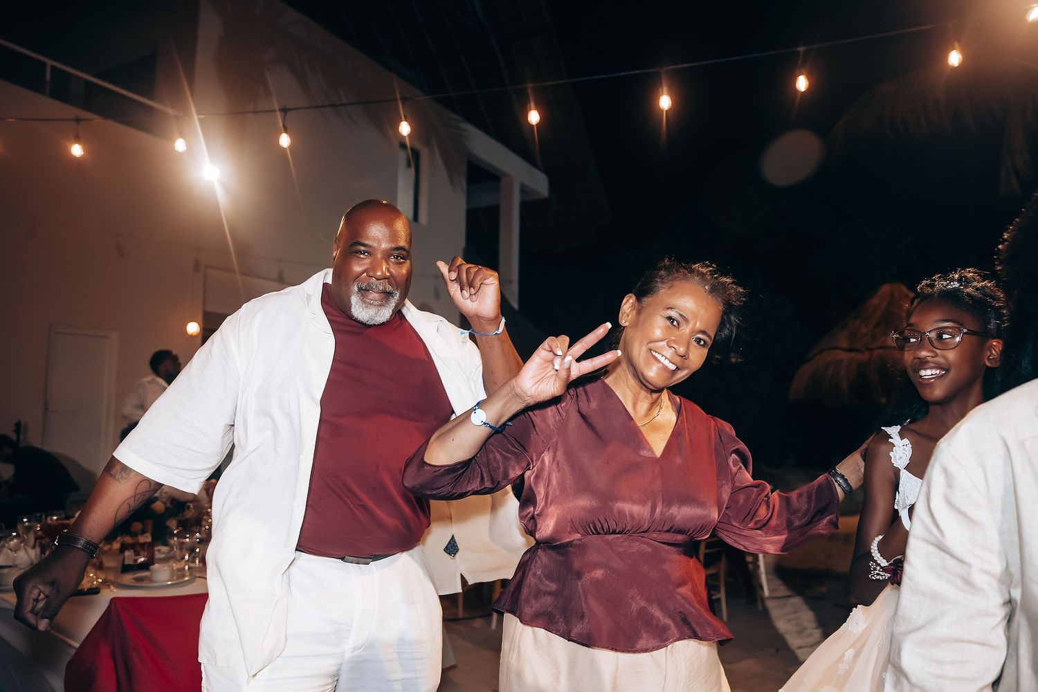 People dance and celebrate together at a dimly lit party with string lights overhead.