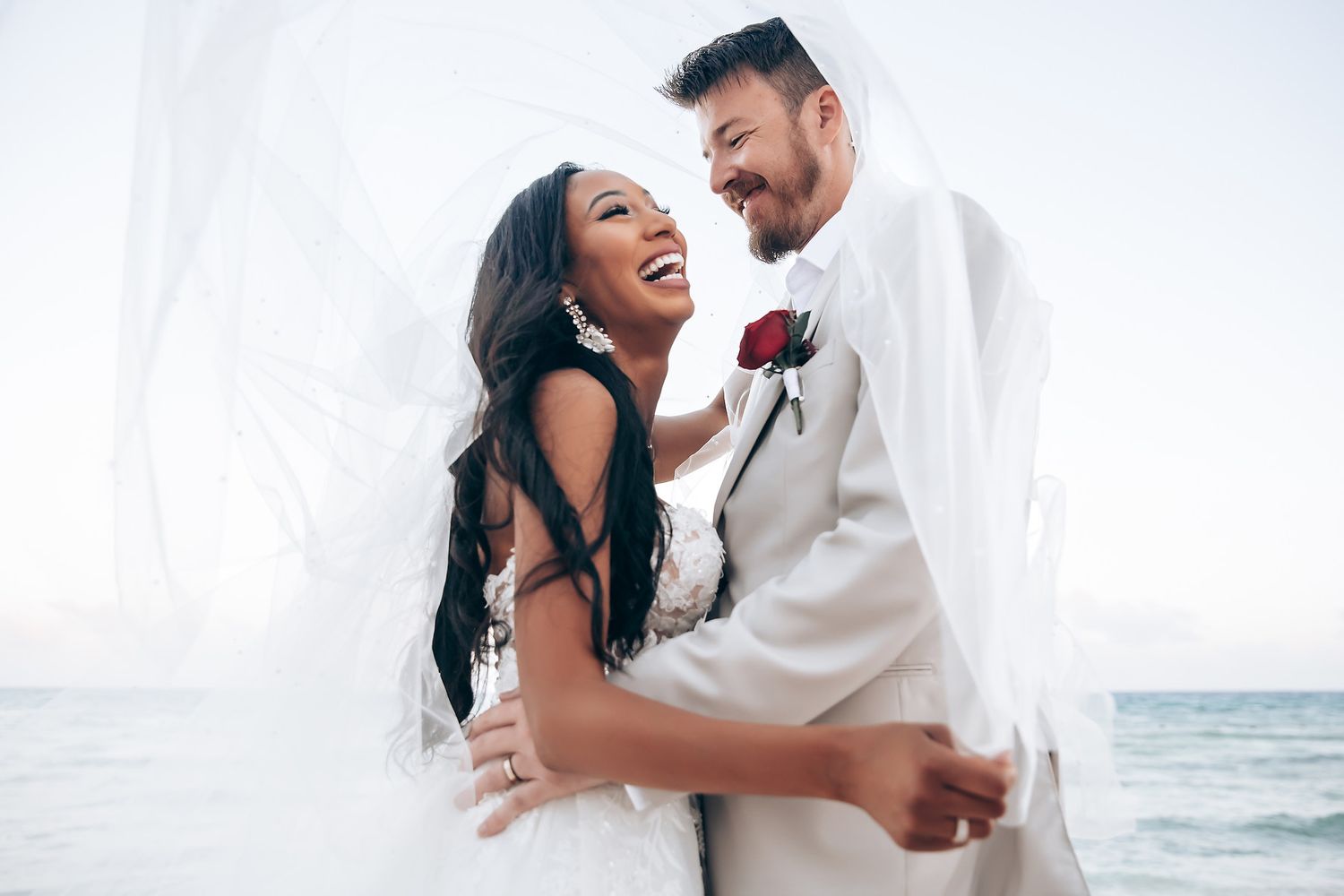 Joyful wedding couple shares intimate moment on beach during sunset photoshoot.