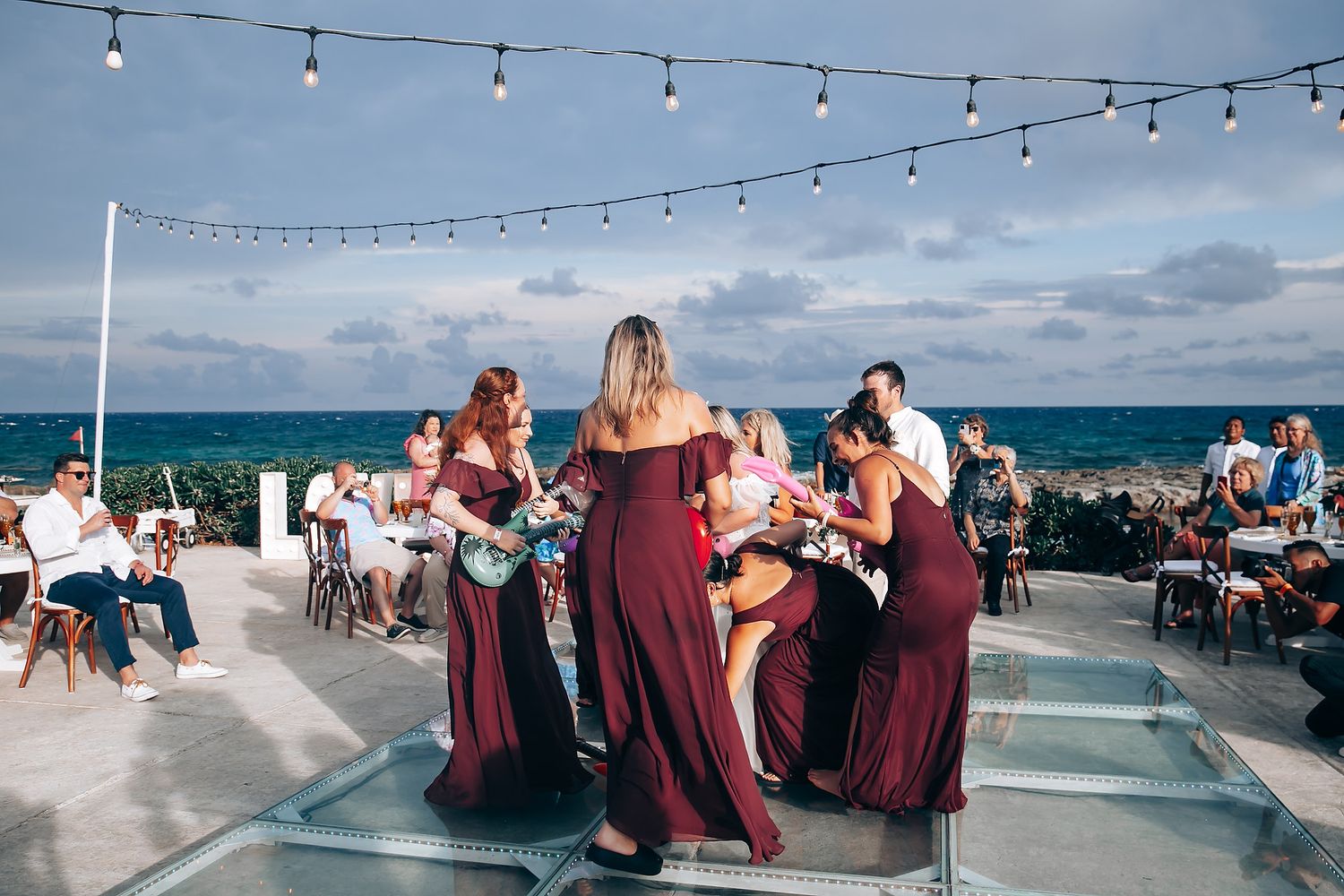 String lights hang over an outdoor wedding reception by the ocean.