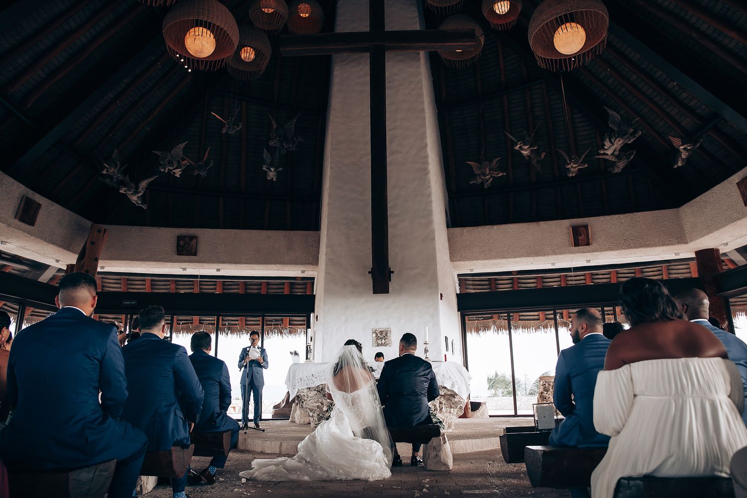Wedding ceremony taking place in a modern octagonal venue with hanging lanterns and wooden beams.