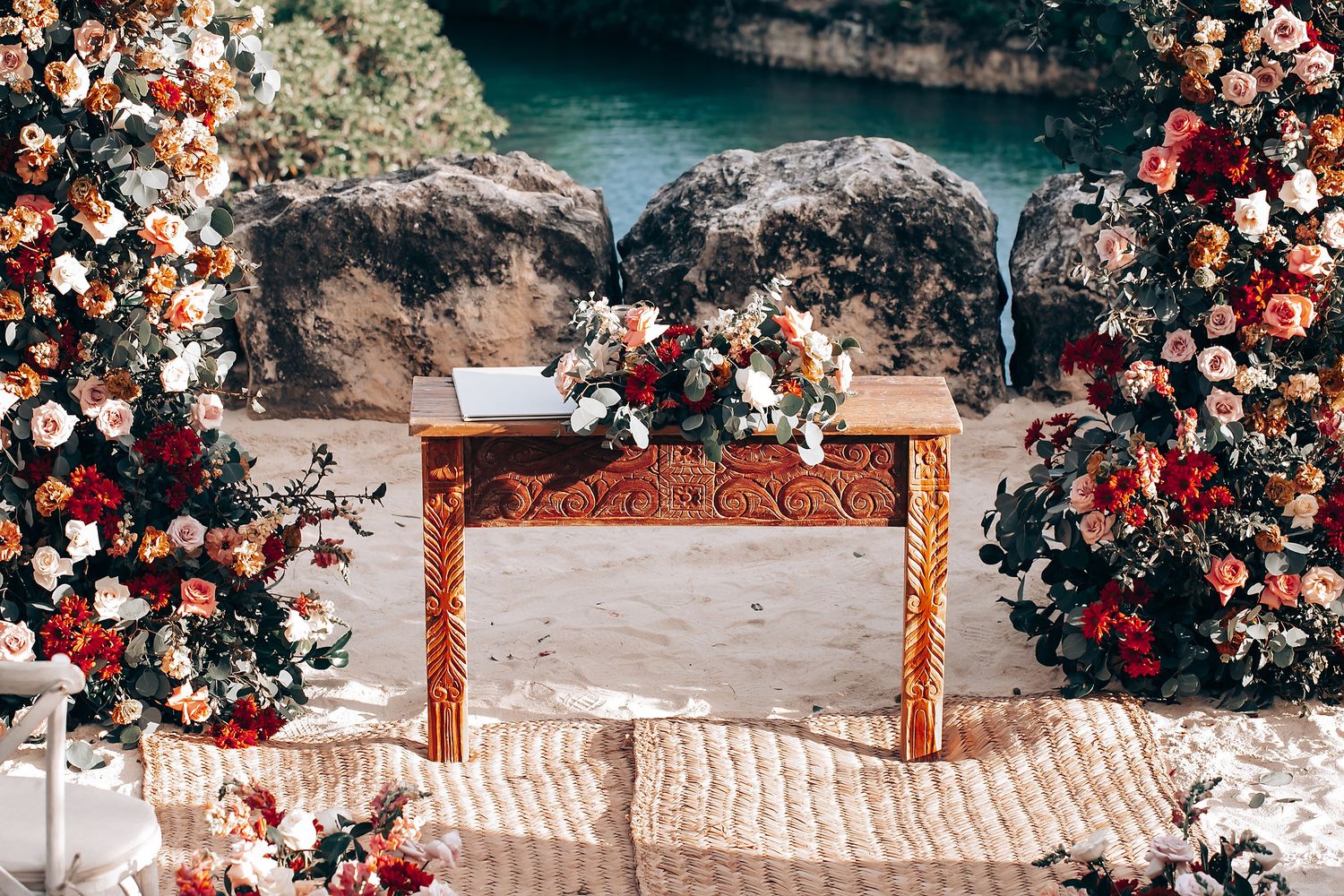 A romantic wedding arch decorated with cascading red and white roses along a stone pathway at sunset.