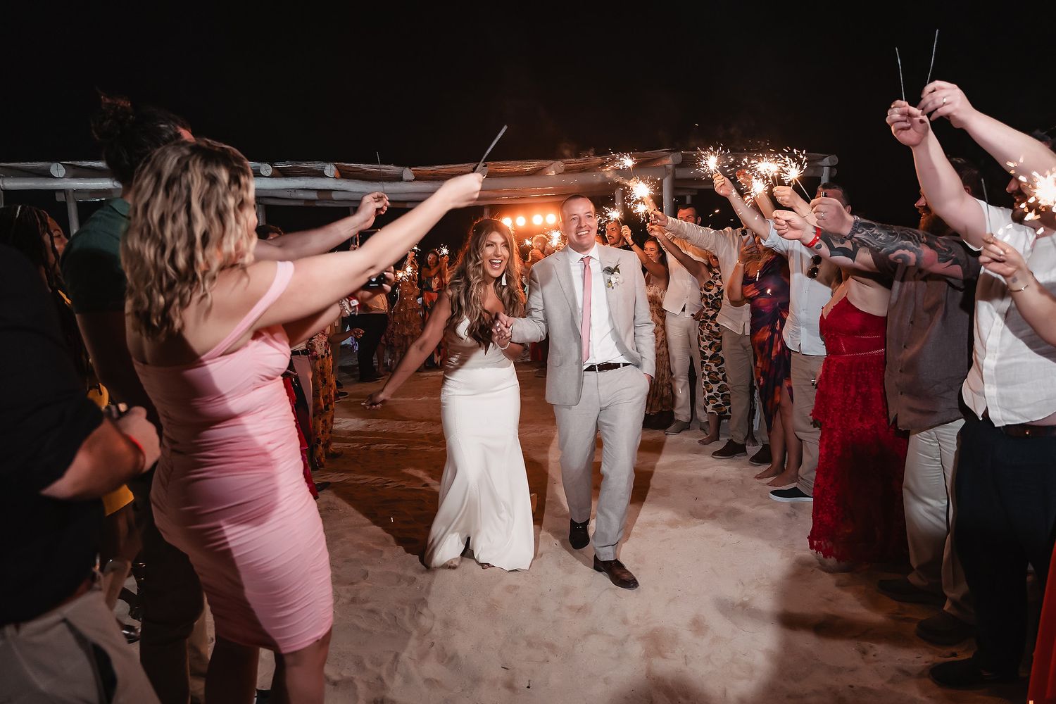 Wedding guests form a tunnel with raised arms as newlyweds walk through during reception.