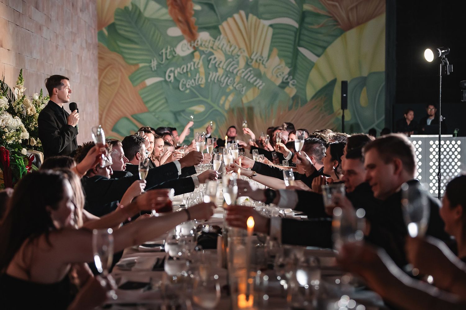 Wedding reception party scene with tropical leaf backdrop and dancing guests.