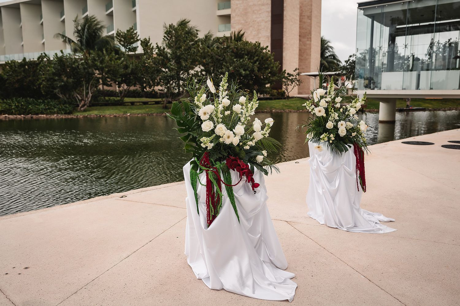 Outdoor wedding ceremony setup with white floral arrangements and chairs along a waterfront venue.