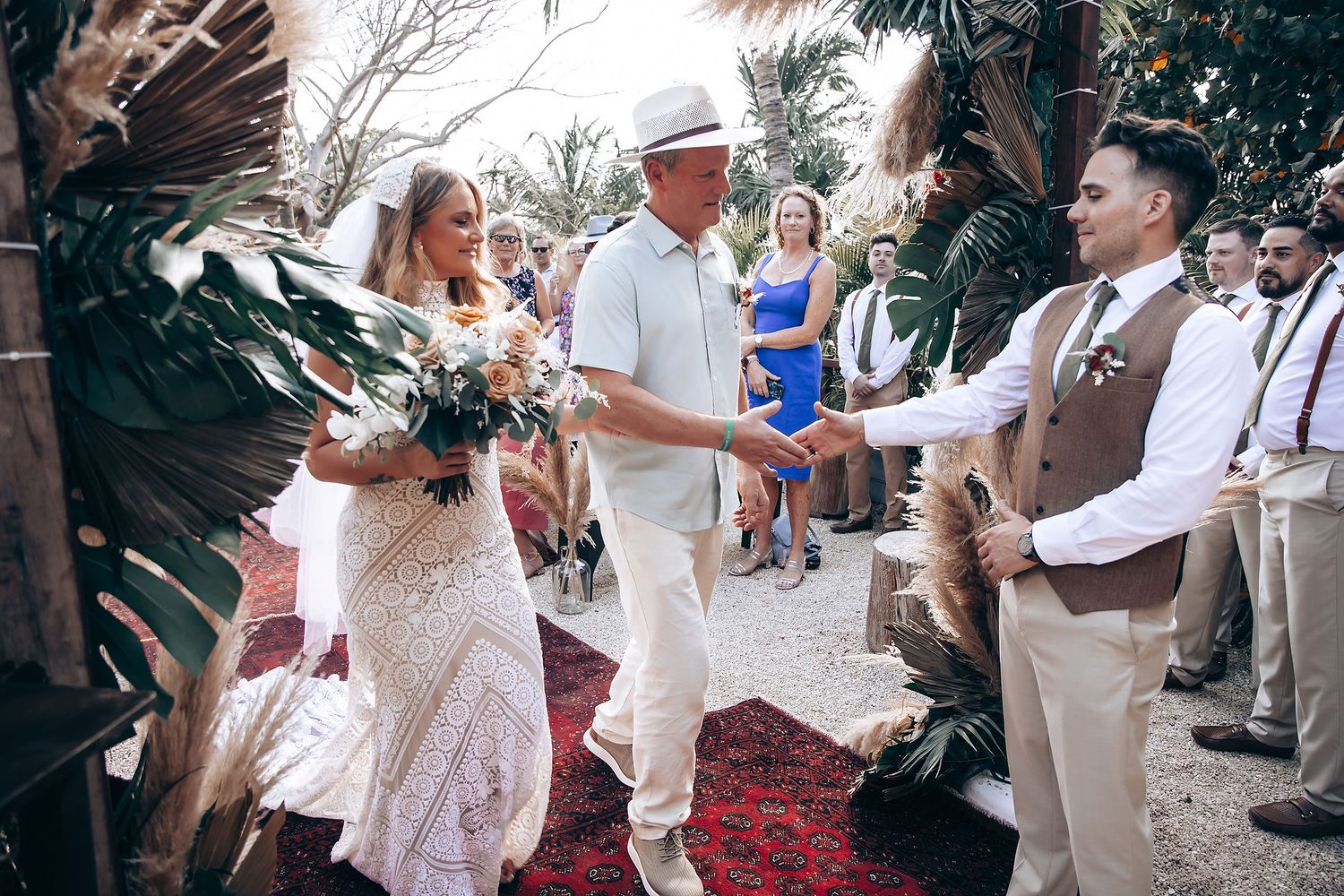 Guests celebrate at an outdoor wedding ceremony decorated with palm trees and boho decor.