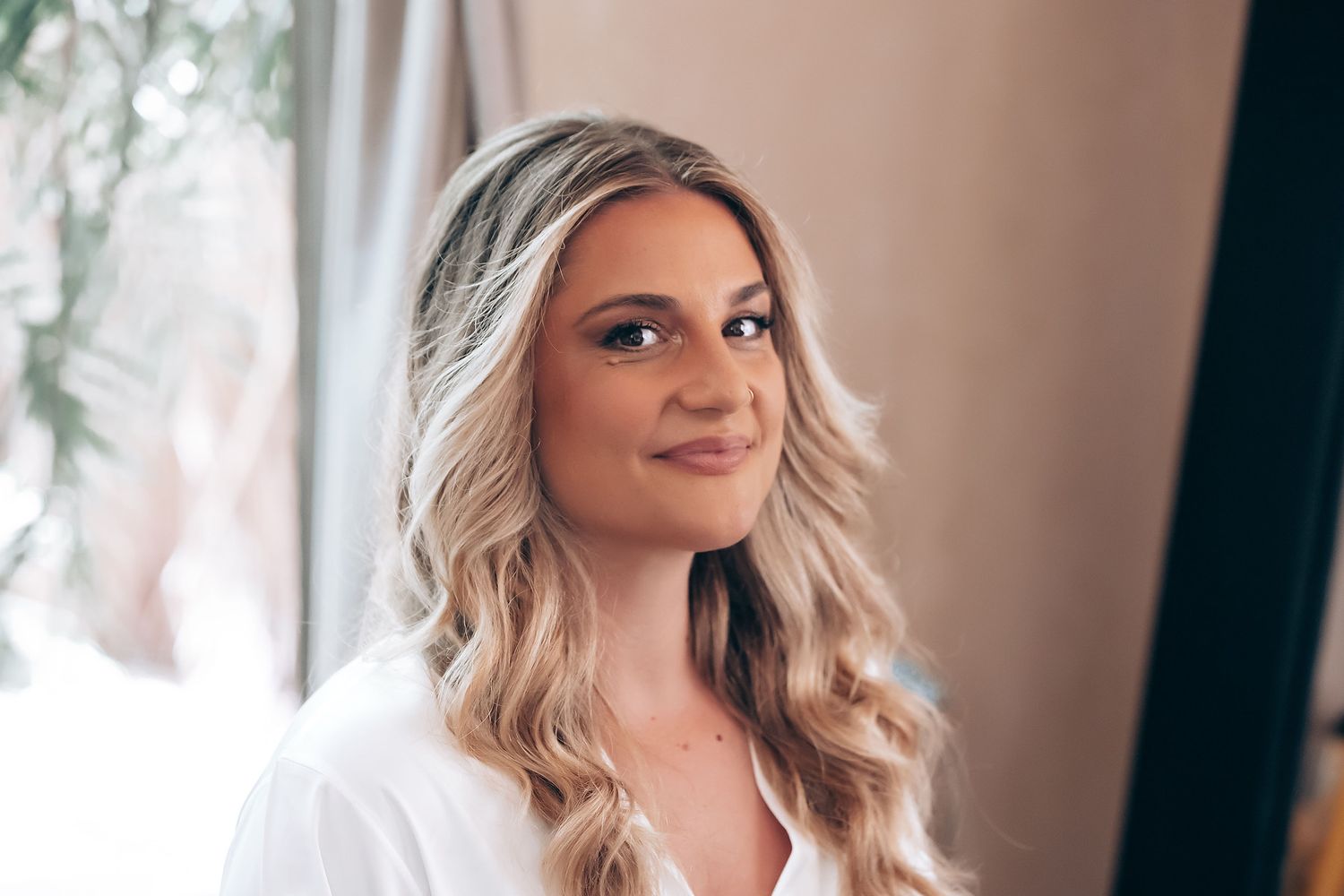 Woman in white dress getting ready for wedding day with soft window lighting and romantic atmosphere.