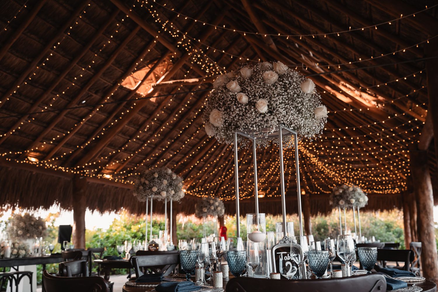 Elegant wedding reception venue with fairy lights draped across a thatched roof and floral centerpieces.
