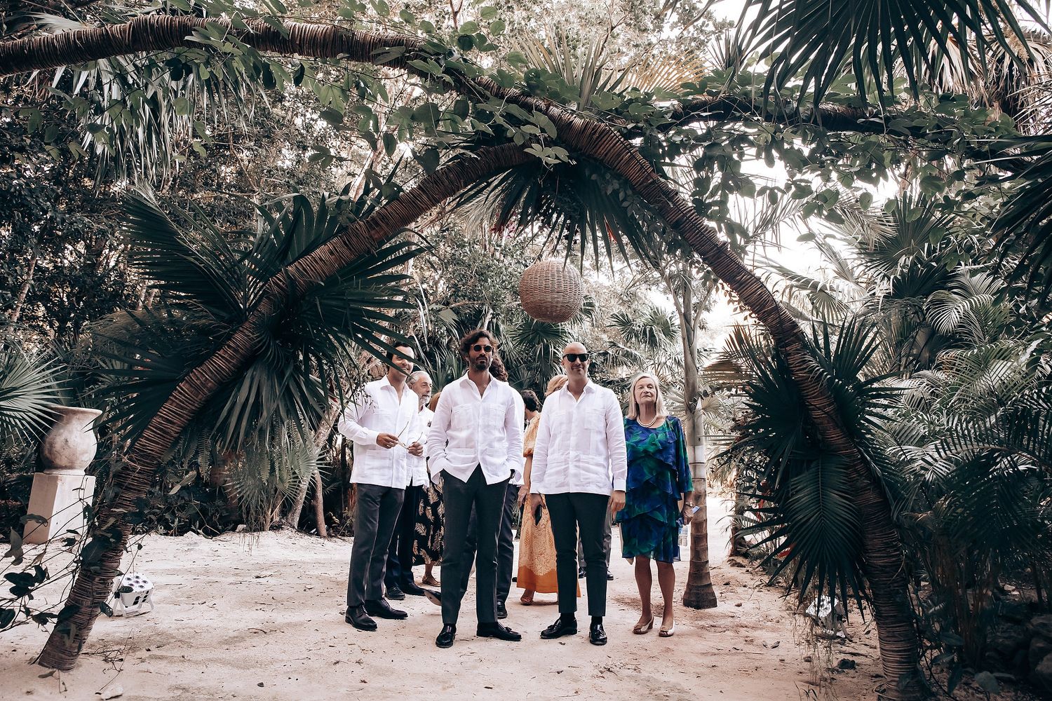 Palm trees line an outdoor wedding ceremony space with guests seated on wooden benches.