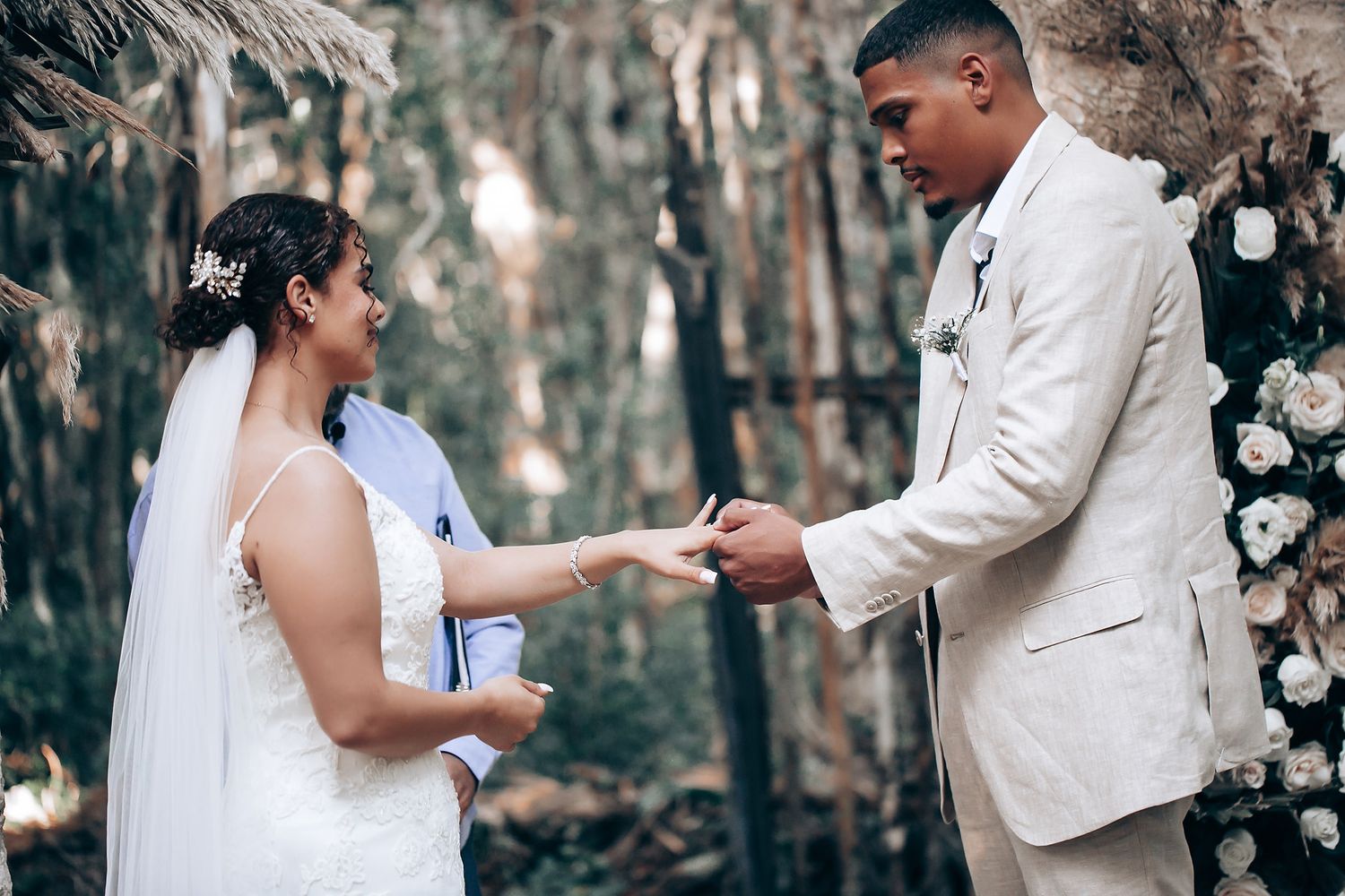 A romantic wedding moment captured in a forest setting with white attire and natural lighting.