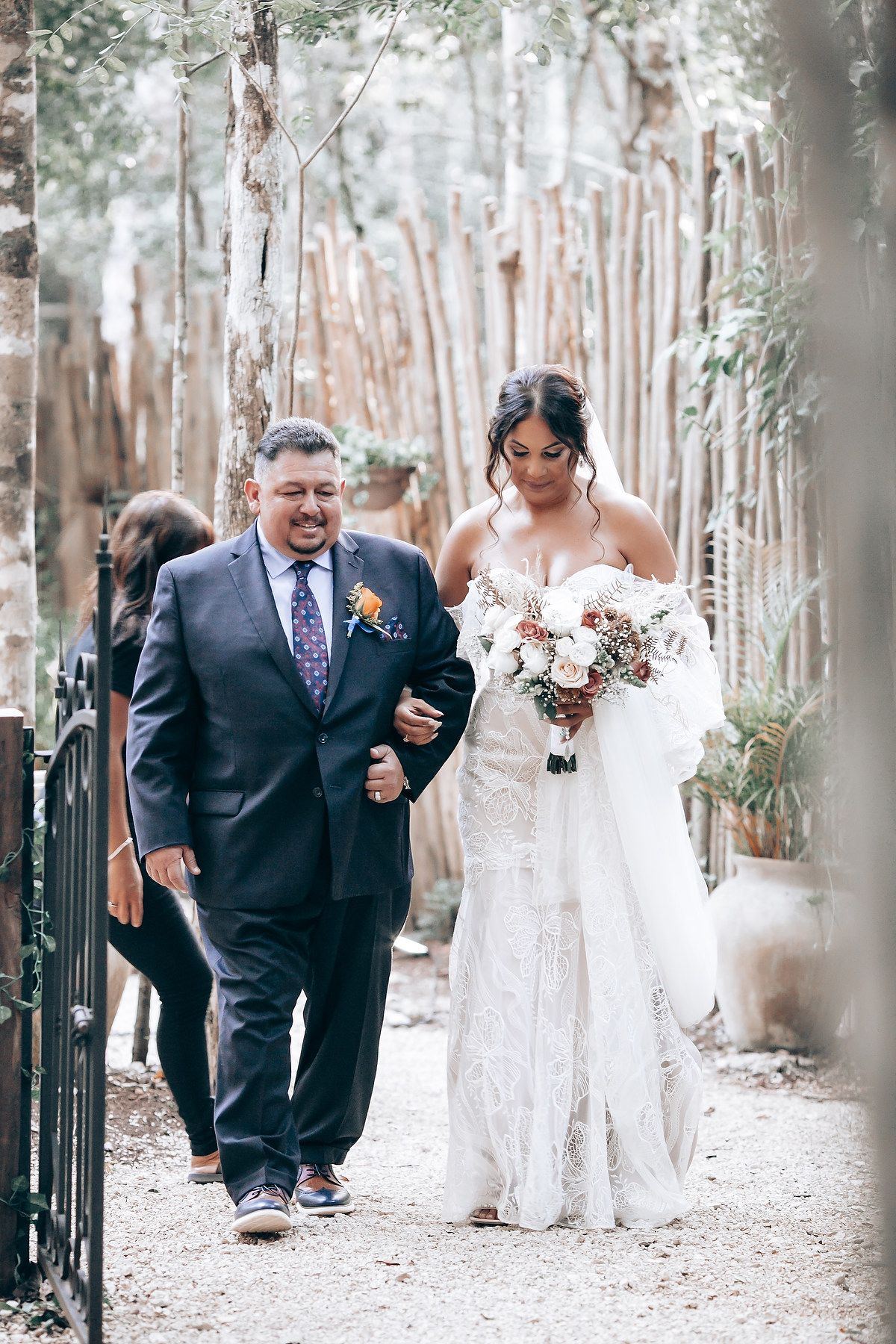 Wedding processional along a tree-lined path with white dress and formal attire.