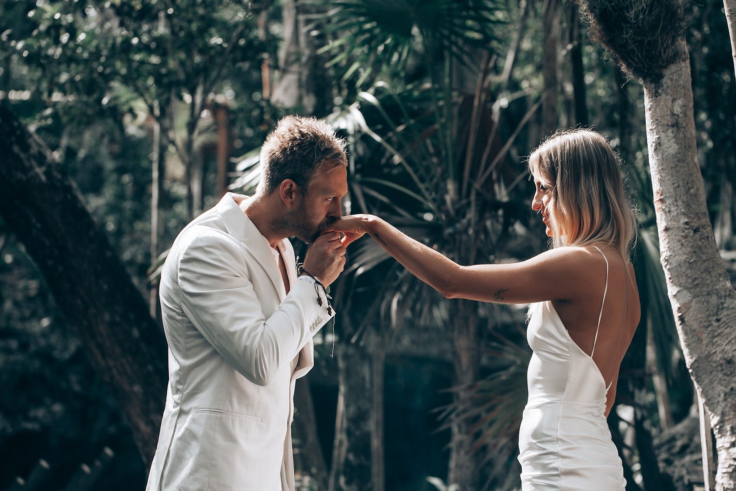 A tender moment captured between a couple in white attire against a forest backdrop.