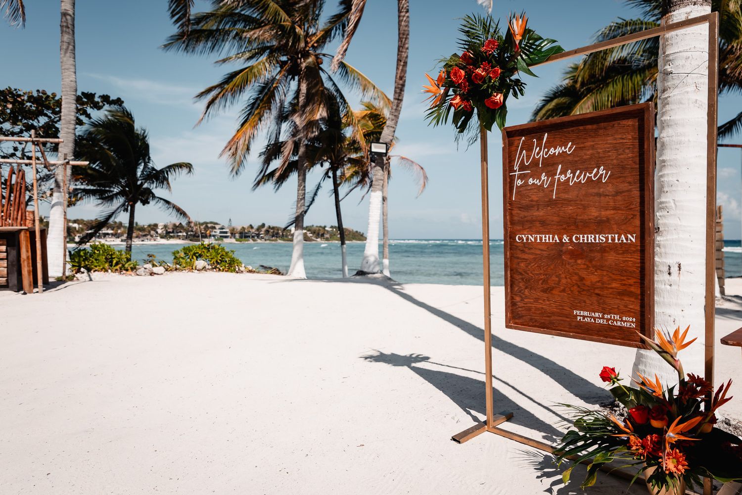 Tropical beach wedding welcome sign for Cynthia and Christian surrounded by palm trees and colorful floral arrangements.