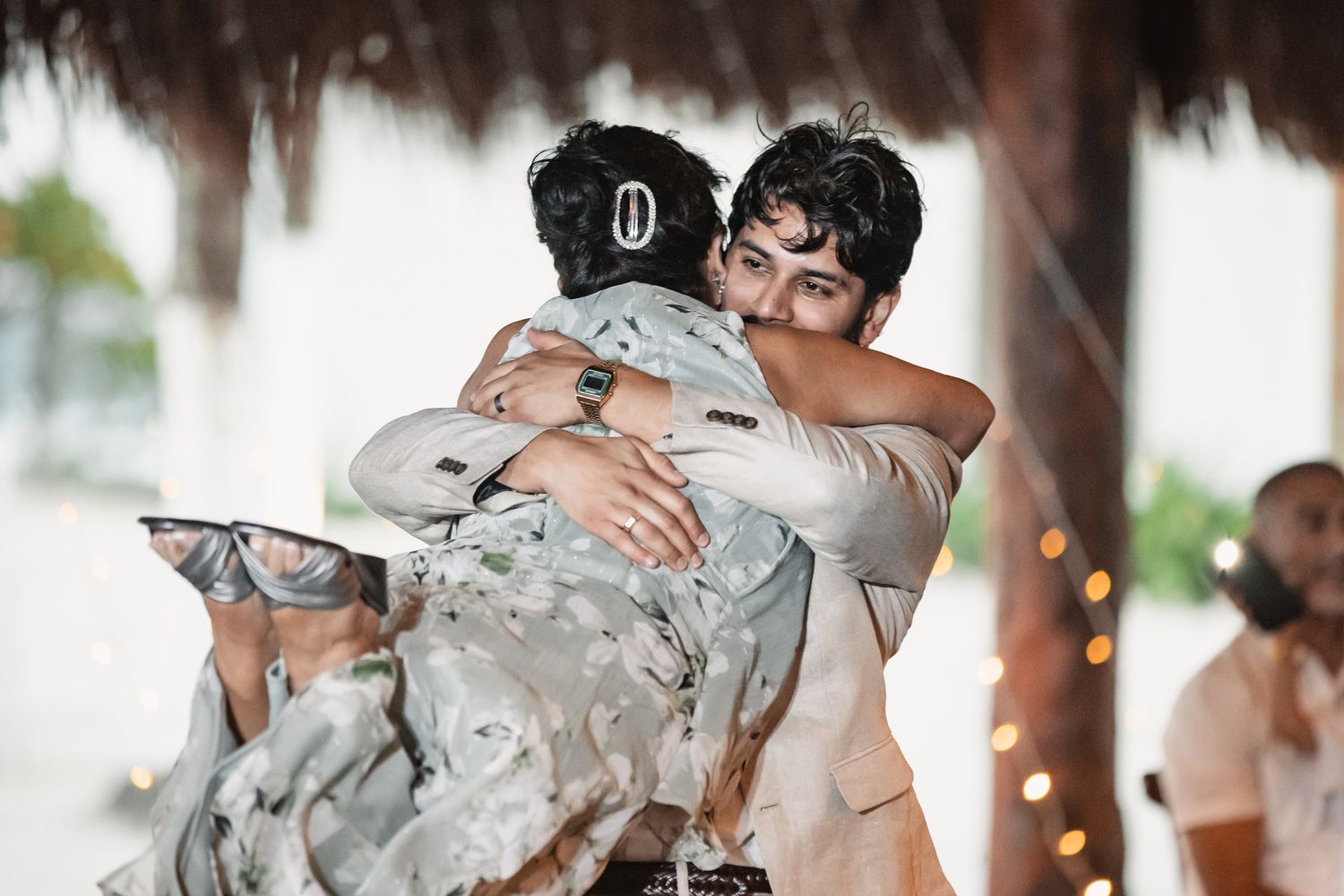 Groom shares heartfelt hug with guest during festive tropical beach wedding reception.