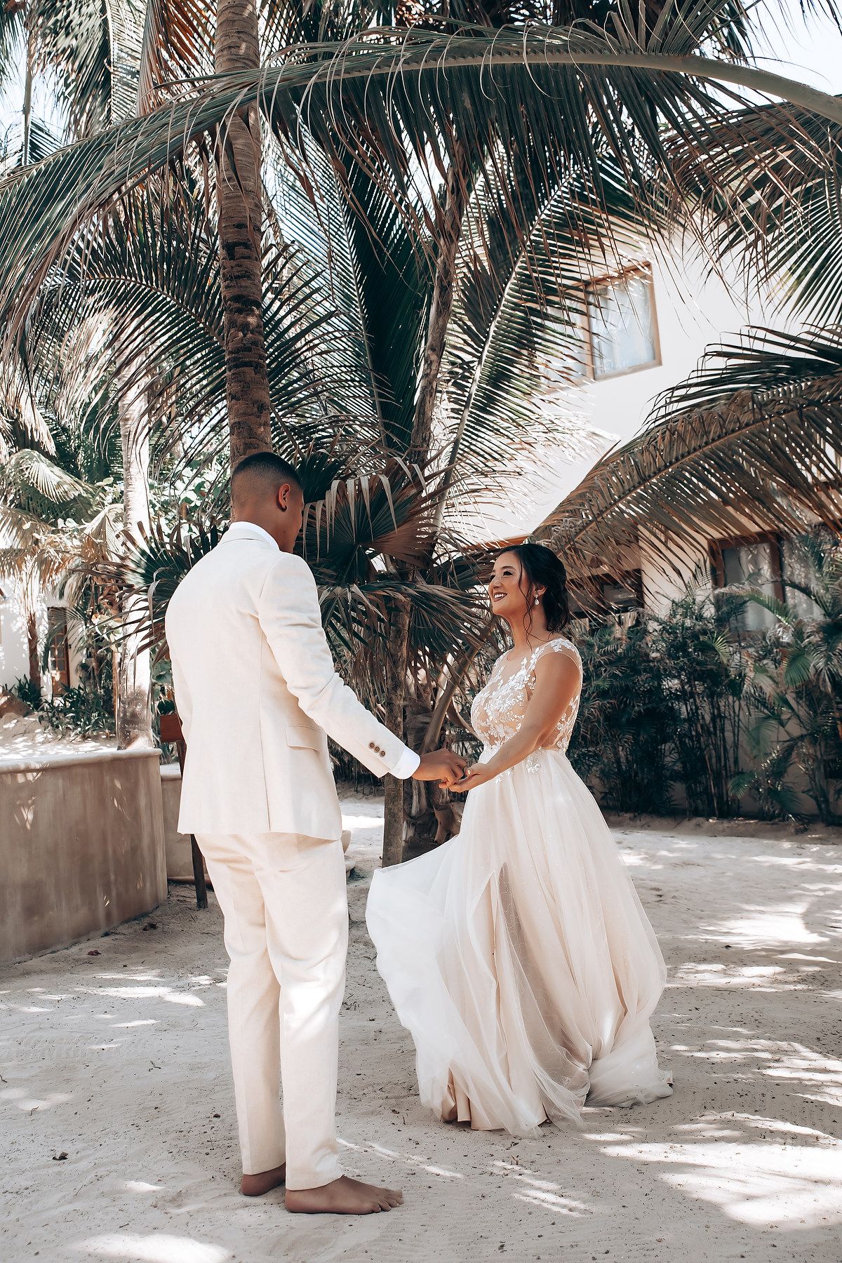 A romantic beach wedding moment with a couple in white attire under swaying palm trees.