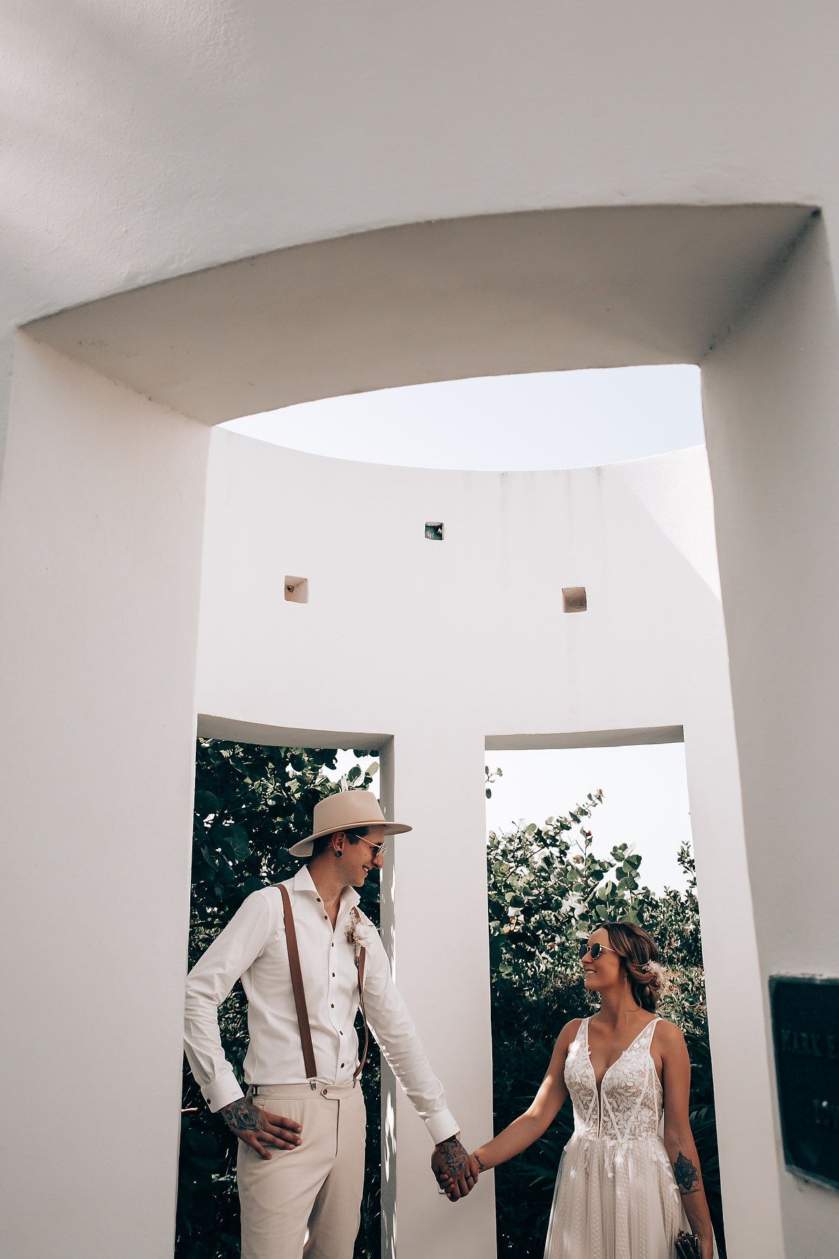 A wedding photoshoot under white architectural arches with tropical foliage in the background.