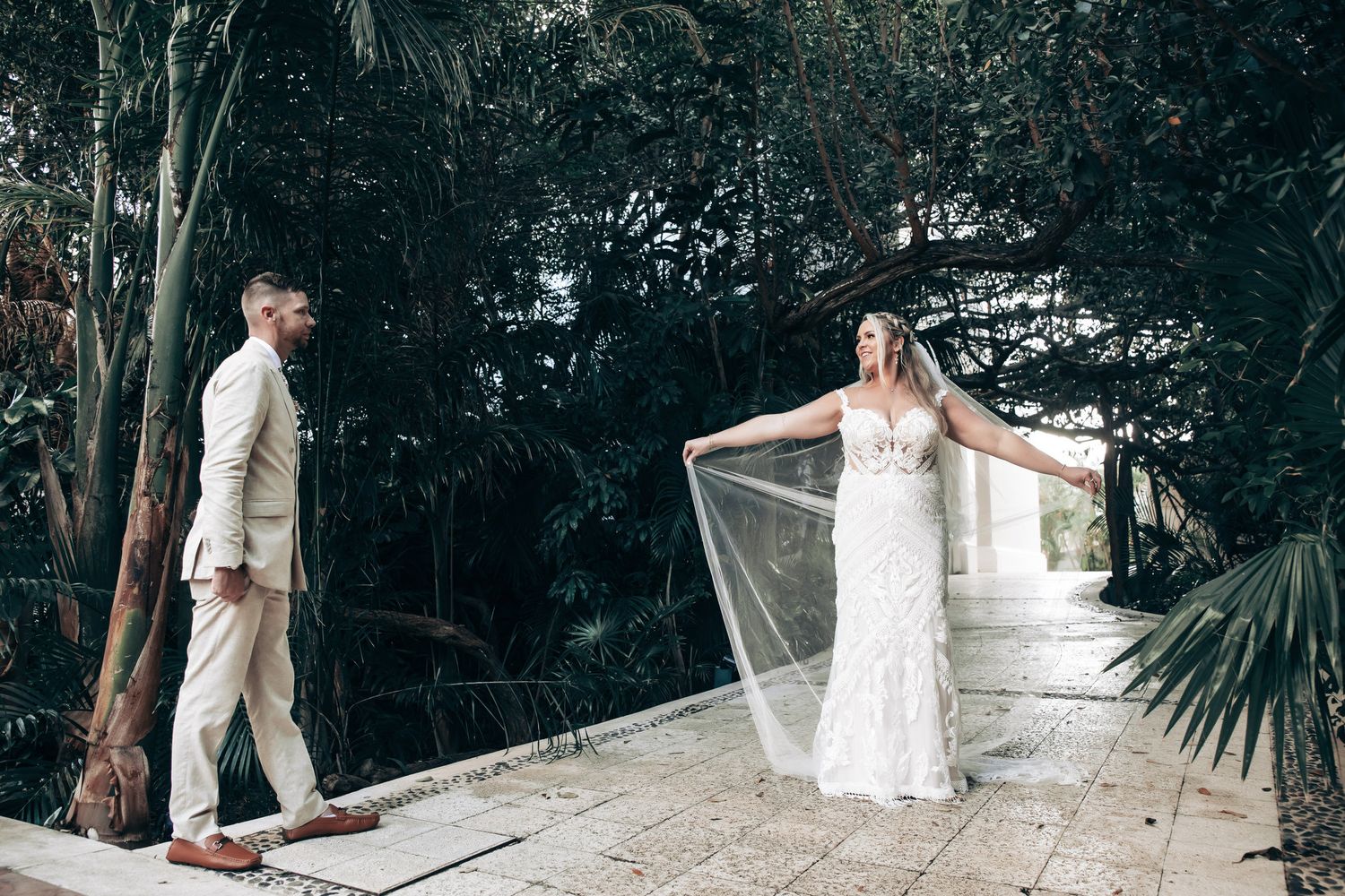 Bride and groom share a first look moment outdoors surrounded by lush tropical greenery.