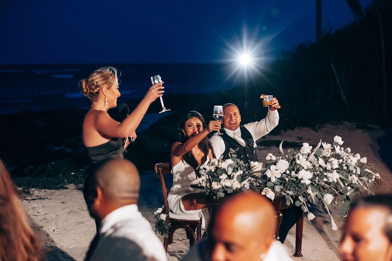 Nighttime beach wedding reception with guests dancing under starlit sky.