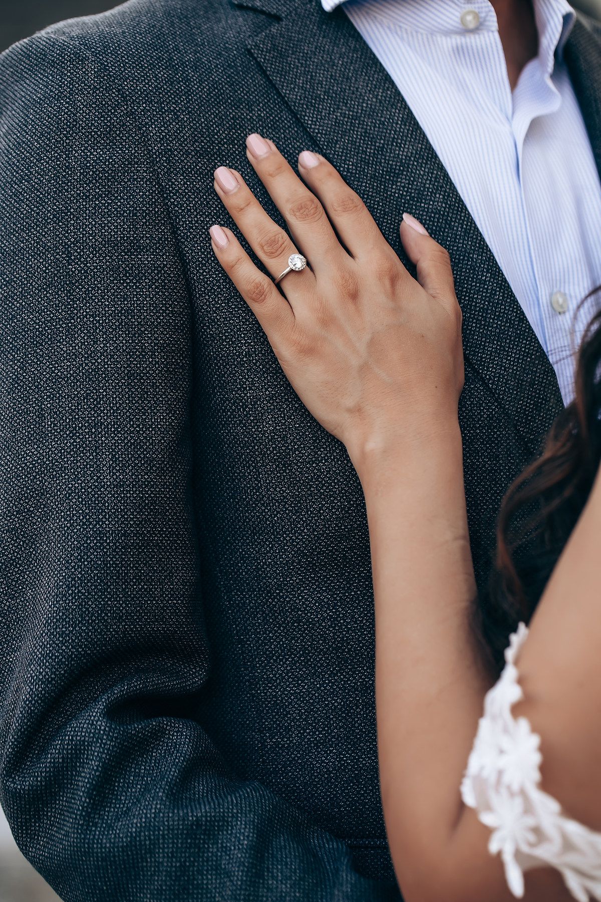 Close-up detail of hands resting on a dark suit jacket with delicate white lace sleeve detail.