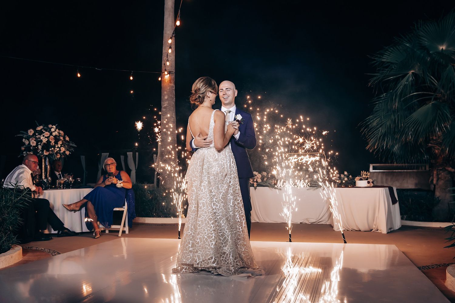 A bride and groom dance together on a lit-up dance floor at their wedding reception with fireworks in the background.