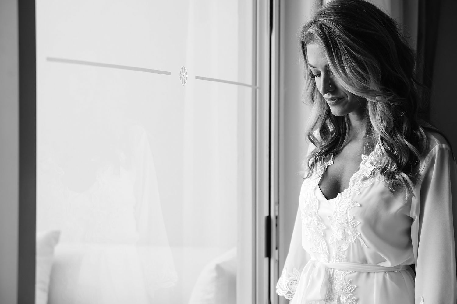 A woman in a white dress stands by a window, looking pensive.