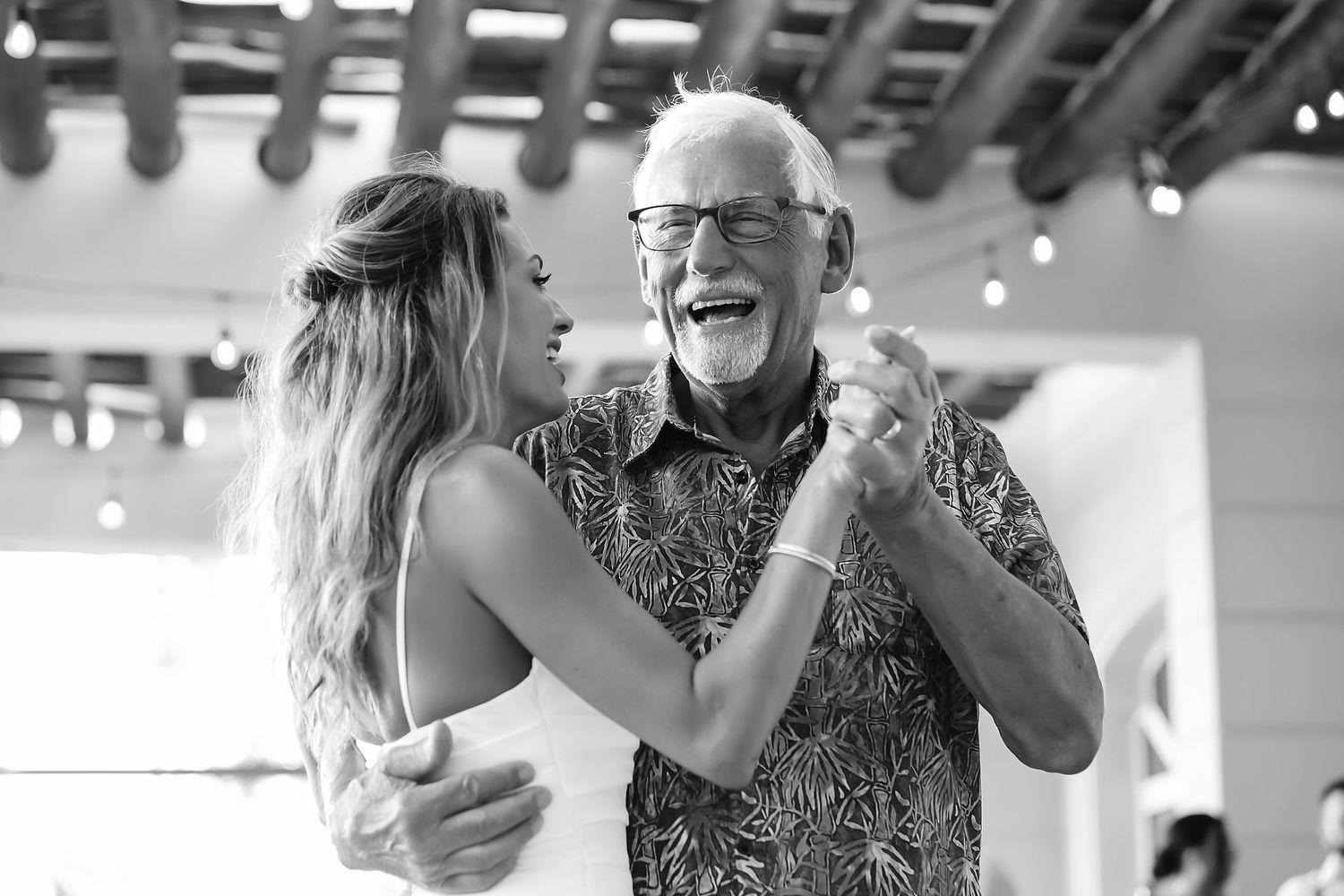 An elderly man and a younger woman dance together at a celebration.