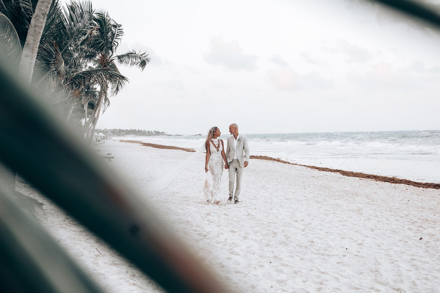 A couple walking along a pristine white sandy beach with ocean waves in the background.