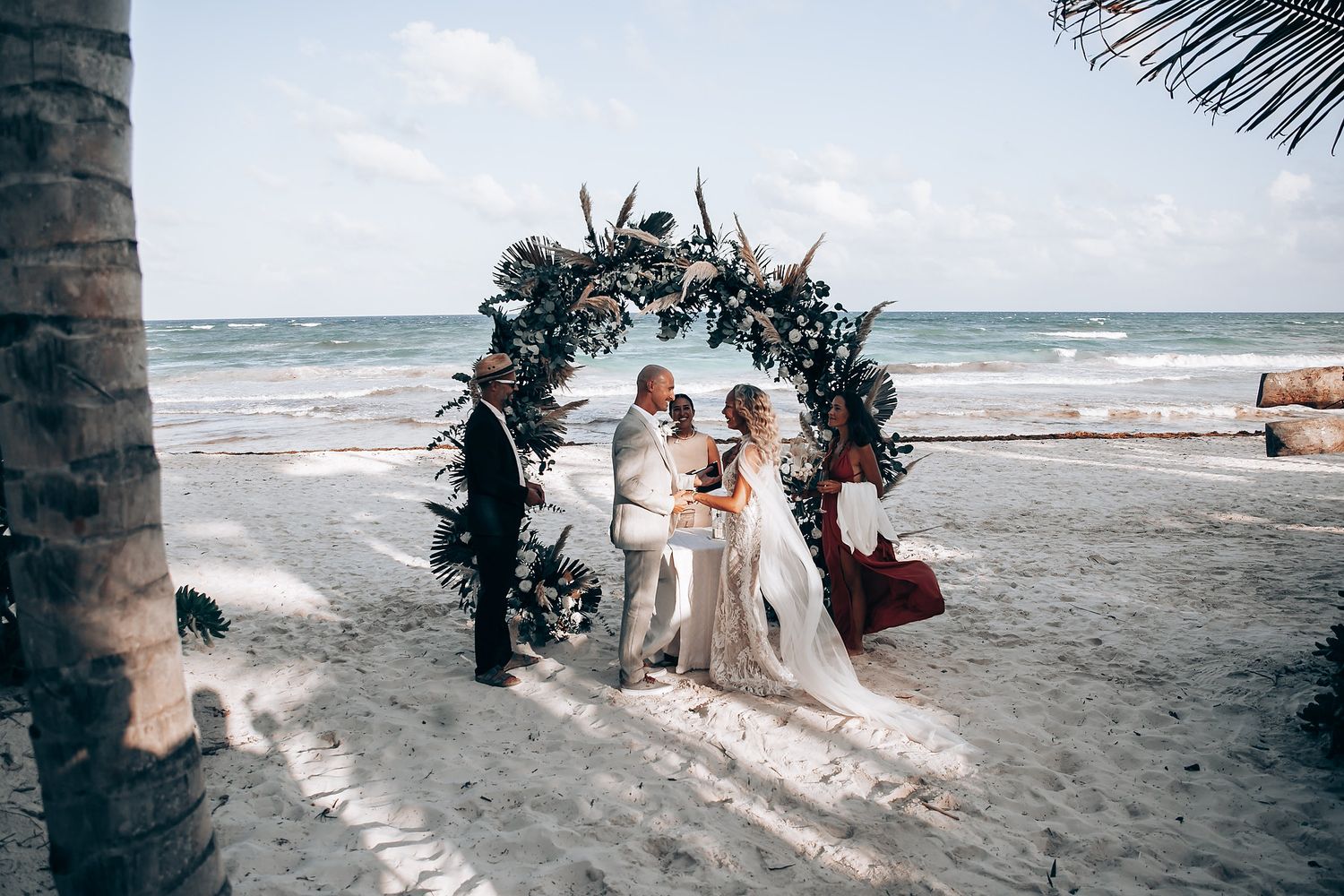 A romantic beach wedding ceremony setup with palm trees and ocean waves in the background.