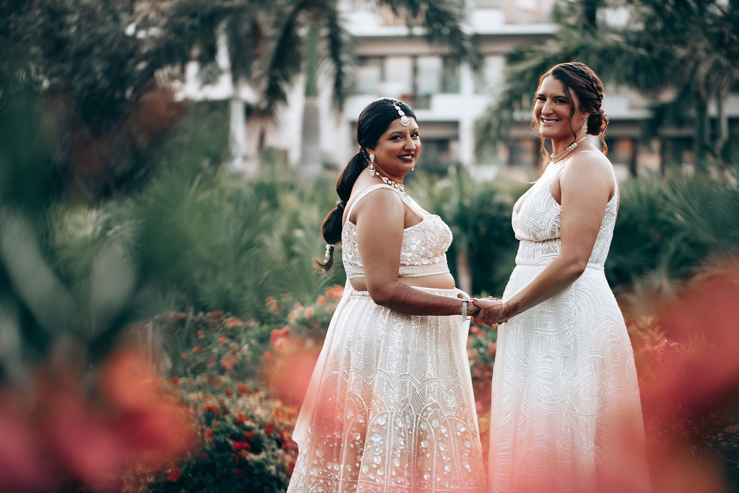 Wedding party members in white dresses walking through a garden setting.