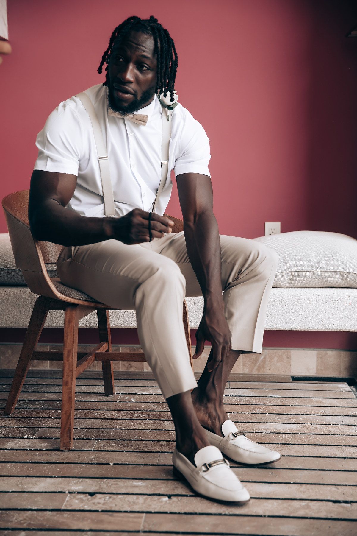 Stylish portrait session showing casual white outfit and sneakers against pink backdrop and wooden floor.
