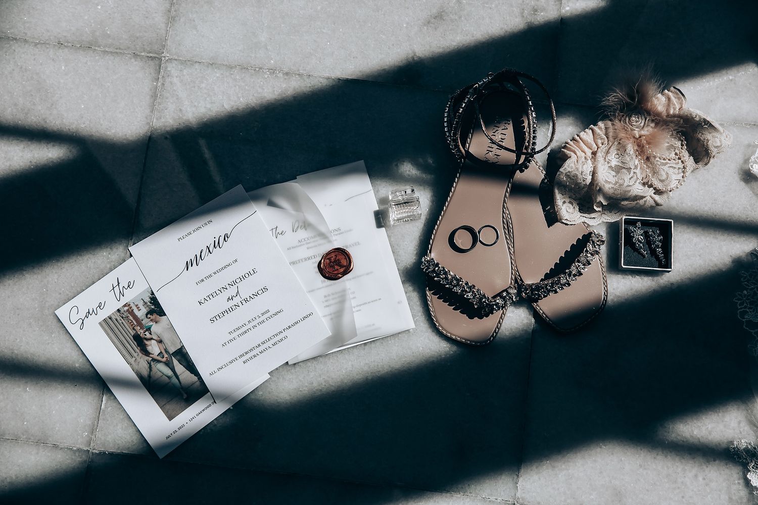 Wedding invitation and black lace lingerie arranged on white surface with dramatic lighting and shadows.
