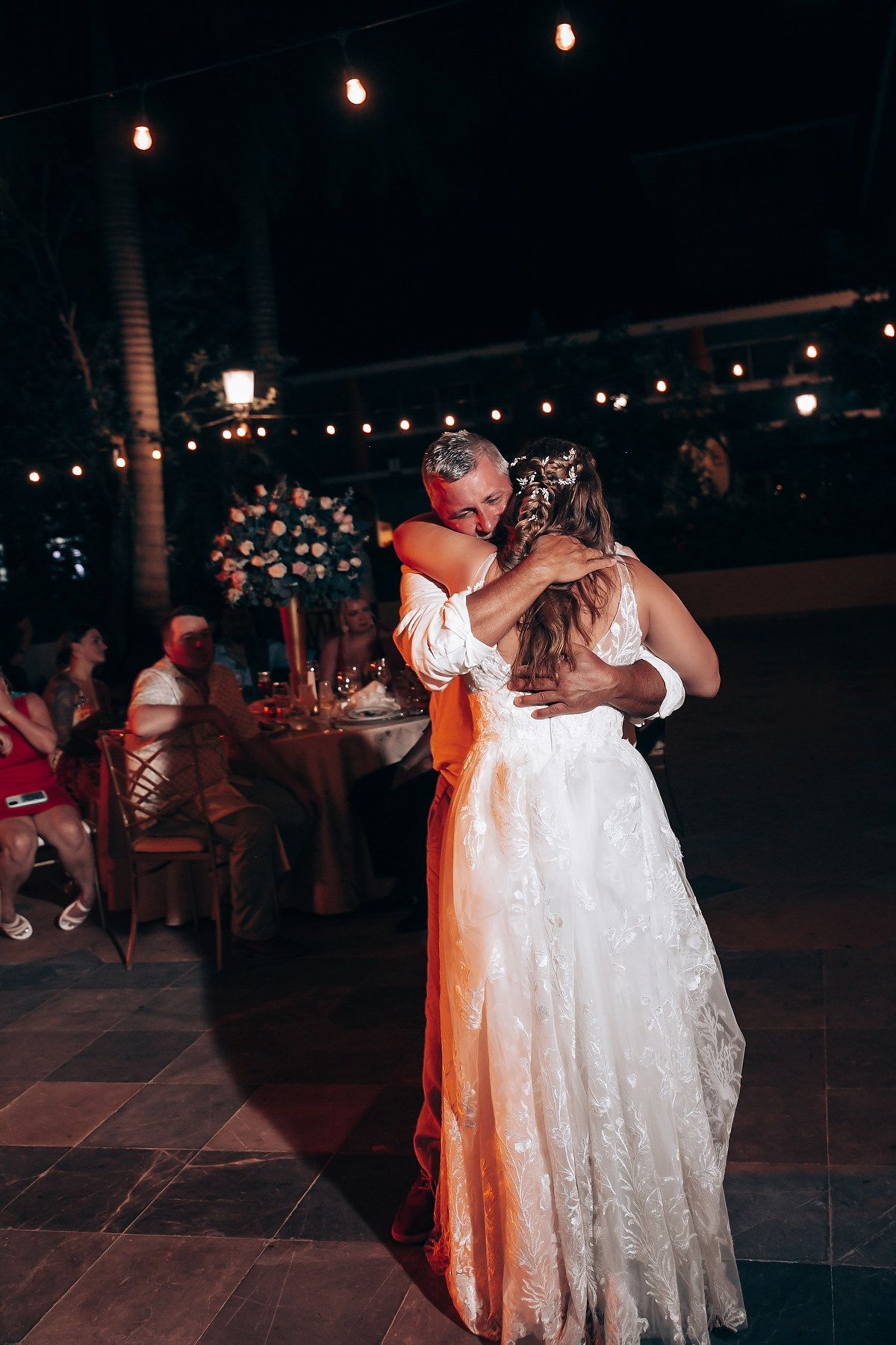 Couple dancing together on an outdoor patio decorated with string lights at night.