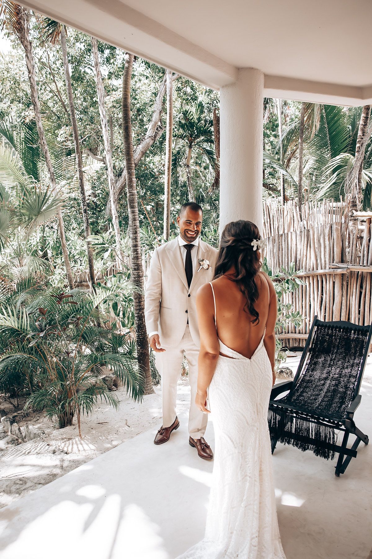 A bright tropical patio with hanging chairs and white pillars overlooking a lush palm garden.