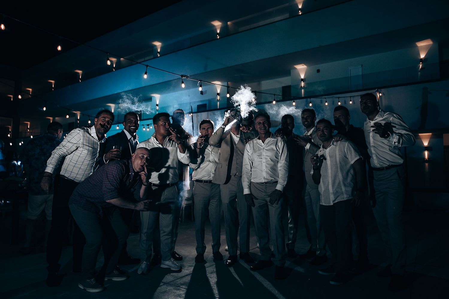 A panoramic view of wedding guests dancing under moody blue lighting at an indoor reception.