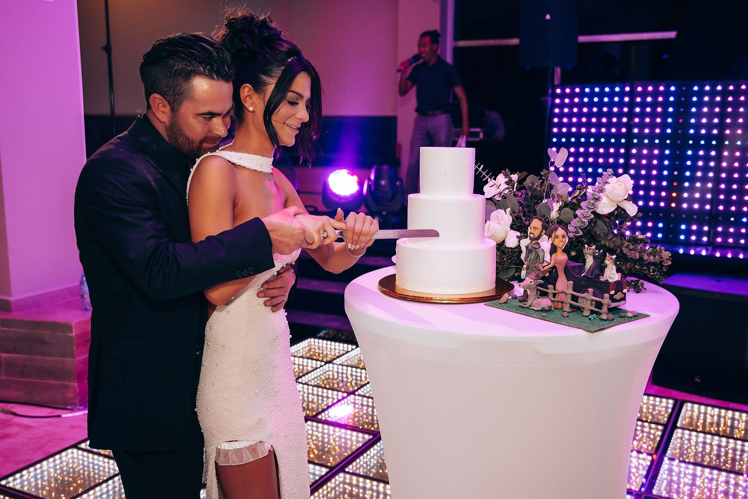 Modern wedding reception with LED lighting and white cake display on illuminated table.