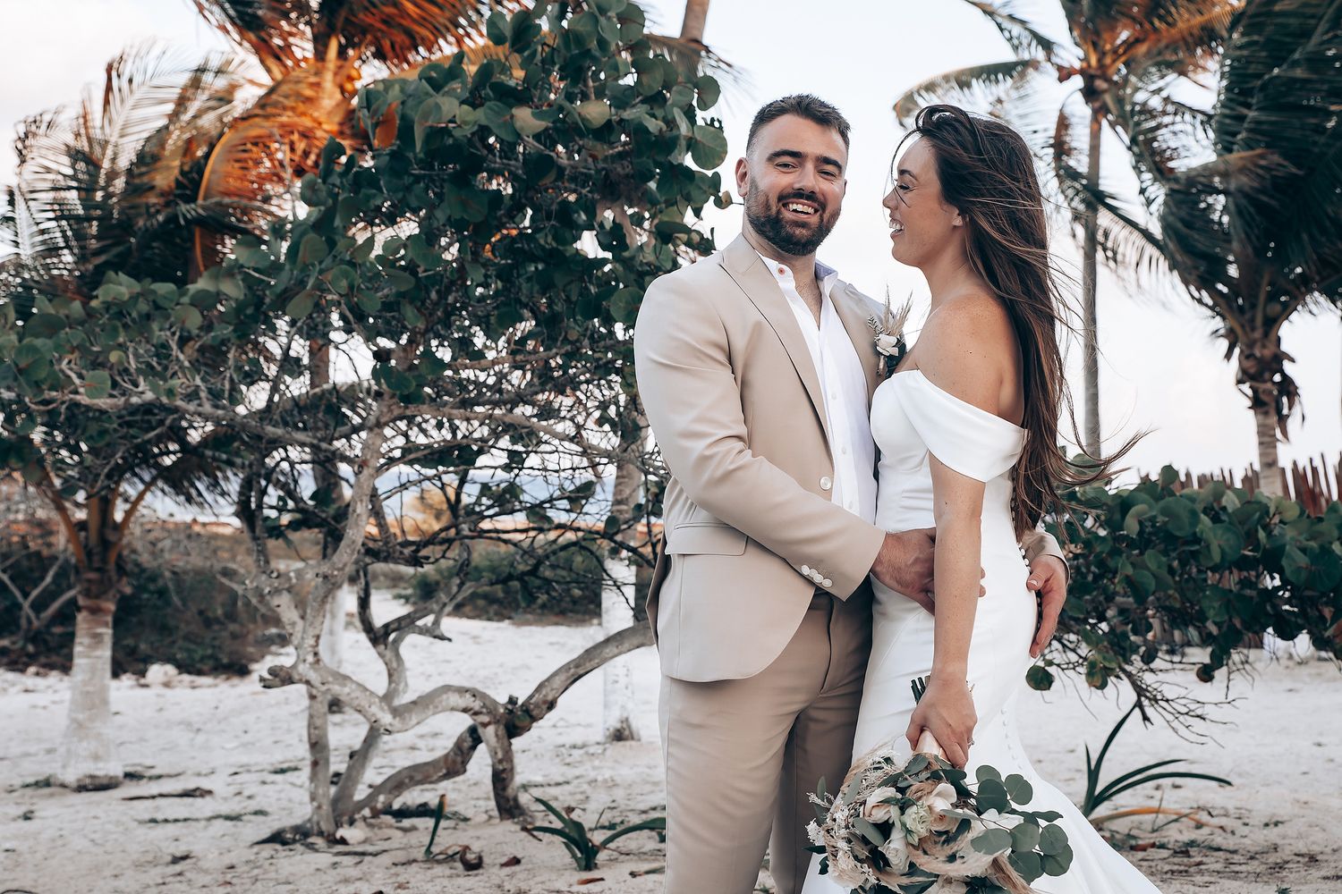 Beach wedding ceremony with elegant floral arrangements and palm trees in the background.