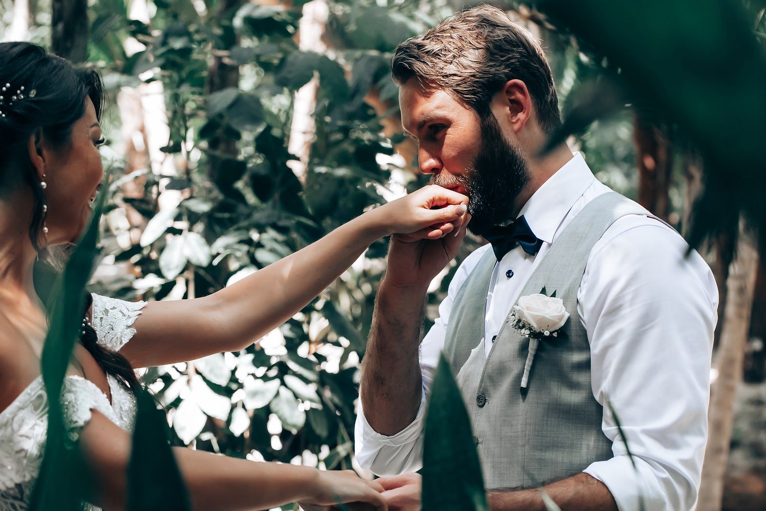 Emotional wedding ceremony moment captured under tropical foliage.