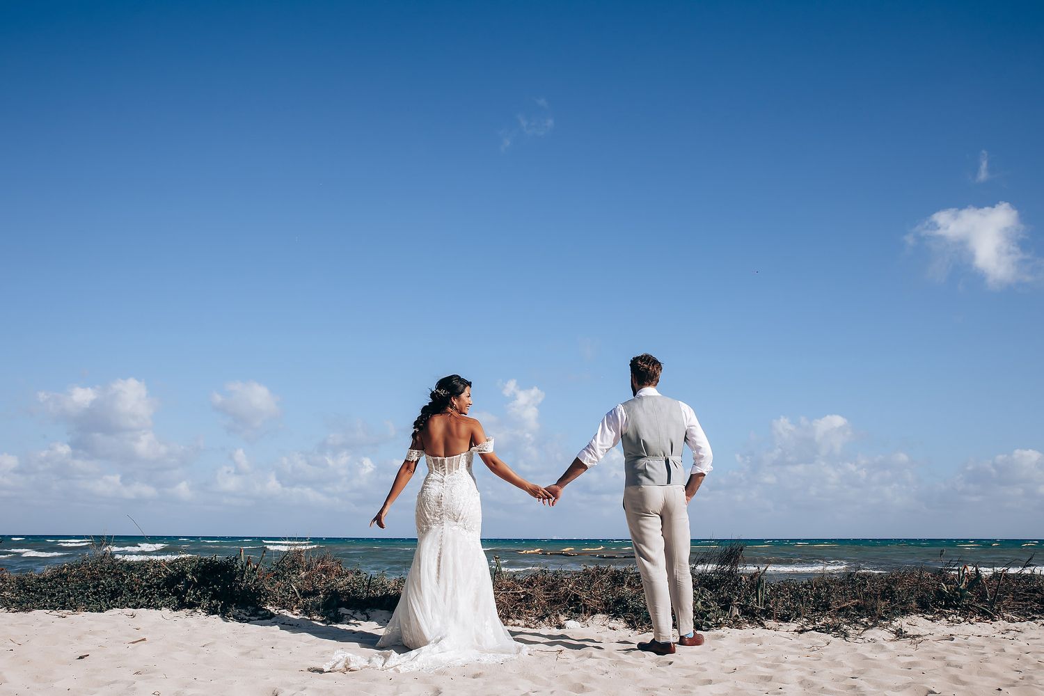 Couple walks hand in hand along pristine white beach with turquoise ocean views.