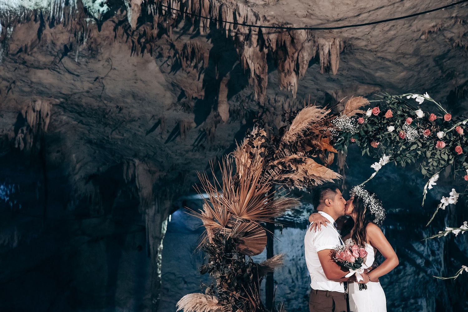 A couple embraces and dances together in a dramatic cave setting with natural rock formations and moody lighting.