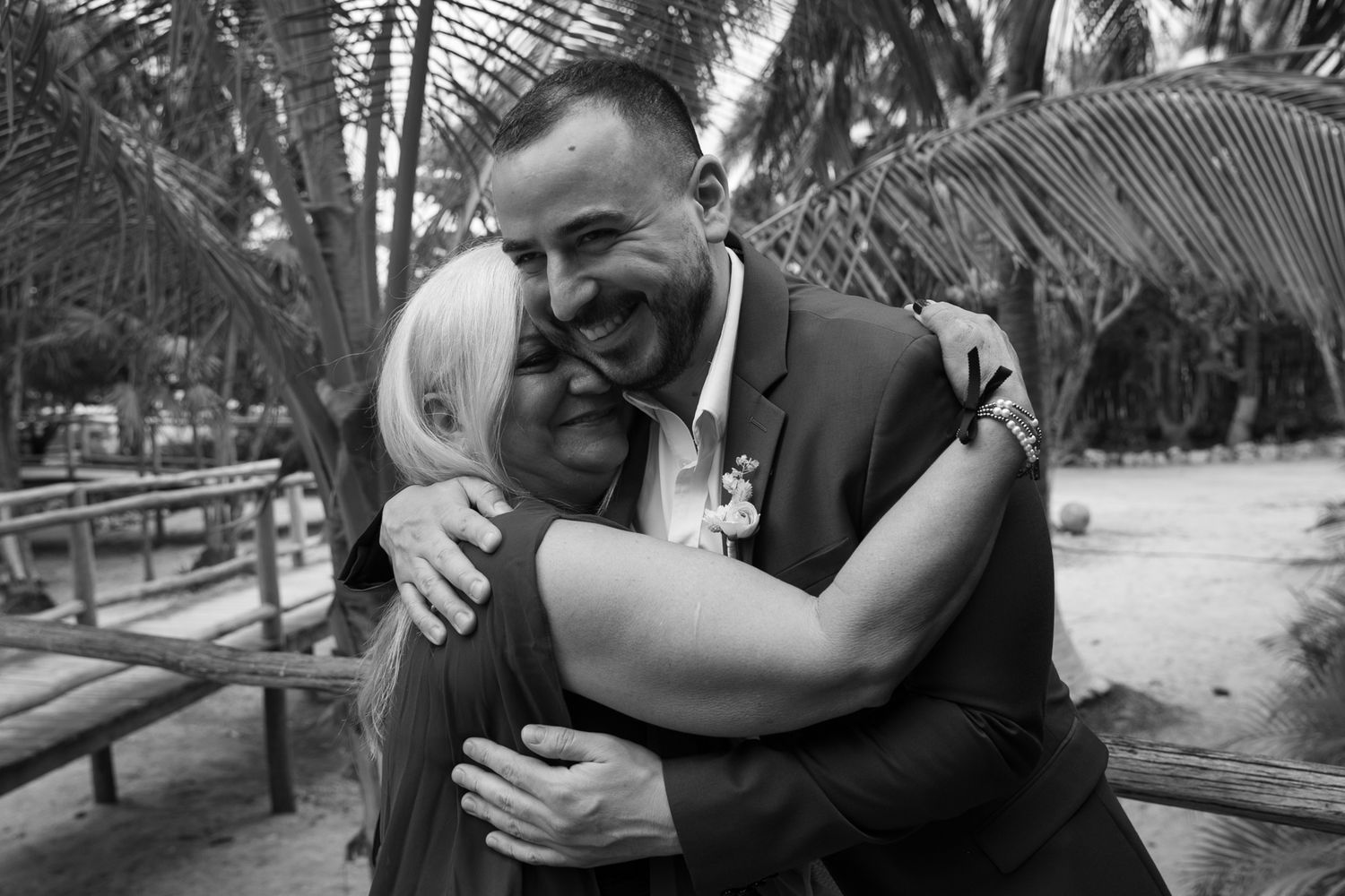 Bride and groom sharing a heartfelt hug outdoors under palm trees in black and white wedding photo.