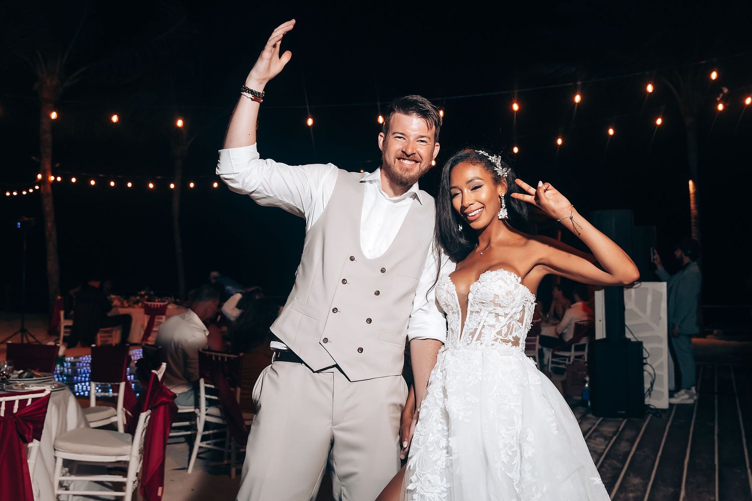 A couple dances joyfully at their wedding reception under string lights on an outdoor deck.
