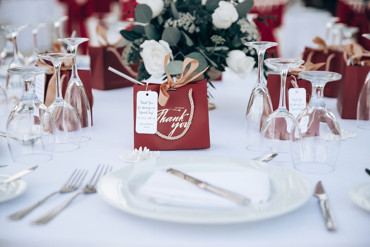 Elegant wedding reception table settings with burgundy and white decor and crystal glassware.