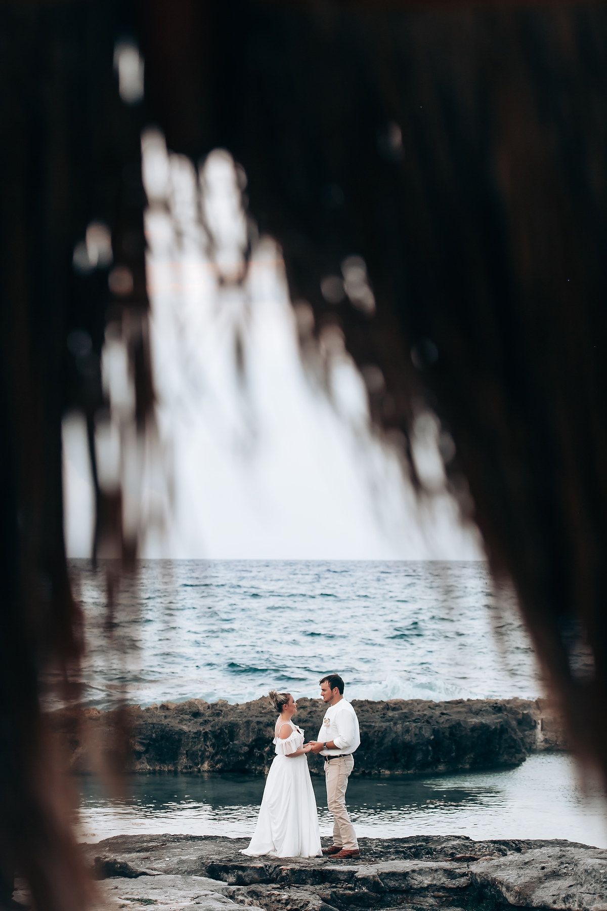 A couple poses on rocky coastal terrain framed by natural elements.