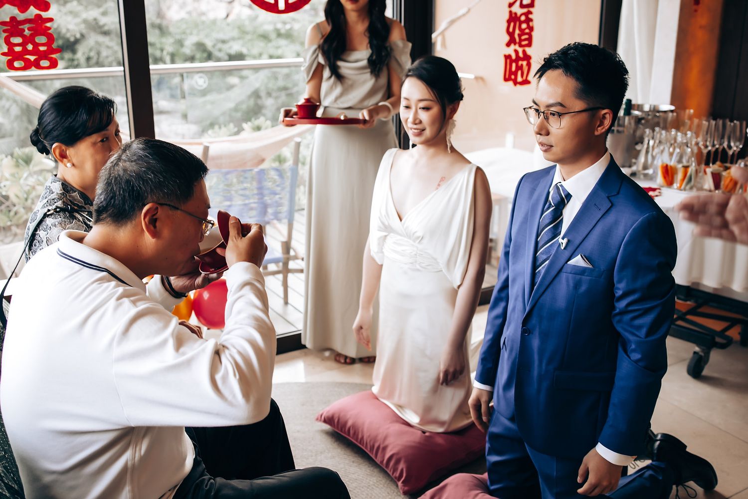 Indoor traditional Chinese wedding ceremony with red decorative elements and natural lighting.