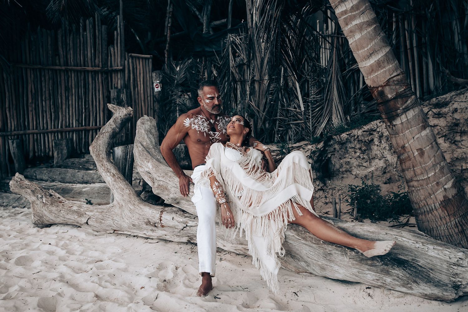A romantic beach photoshoot featuring white flowy clothing and tropical palm trees in the background.