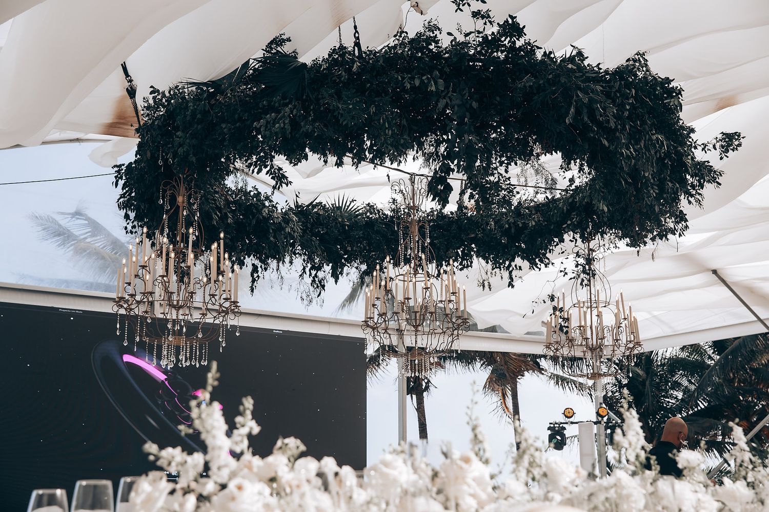 Luxurious crystal chandeliers and white decor at an outdoor wedding reception.