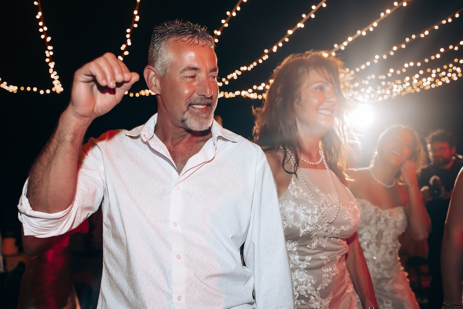 Dancing couple celebrates at their wedding reception under glowing string lights at night.