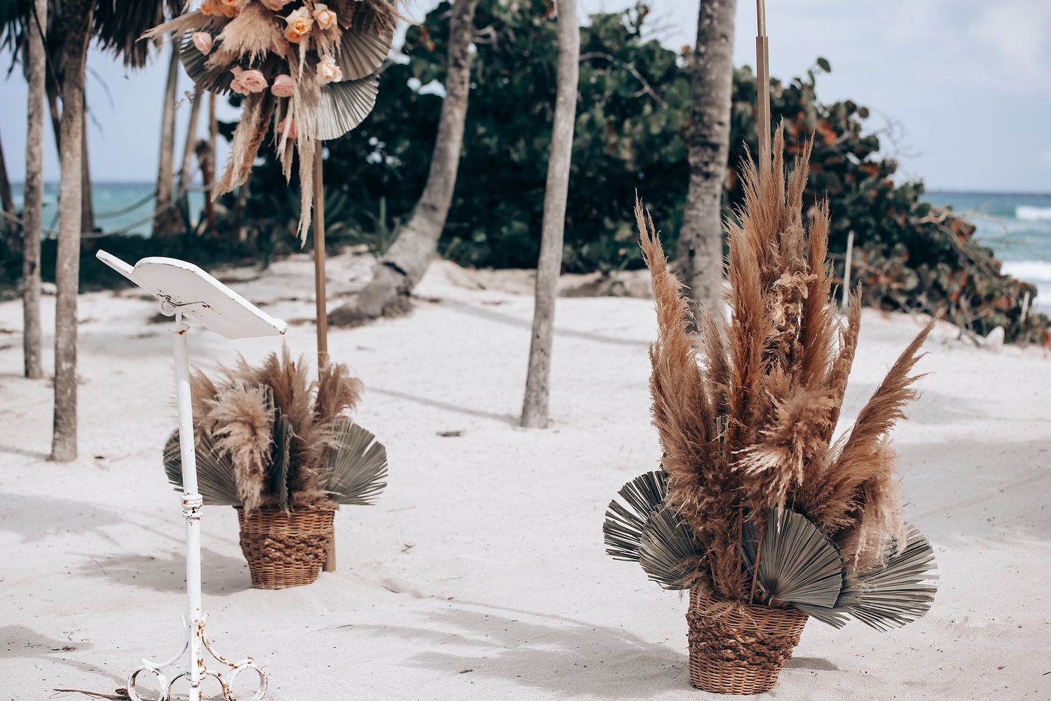 A sandy beach pathway lined with palm trees leads to the ocean on a sunny day.