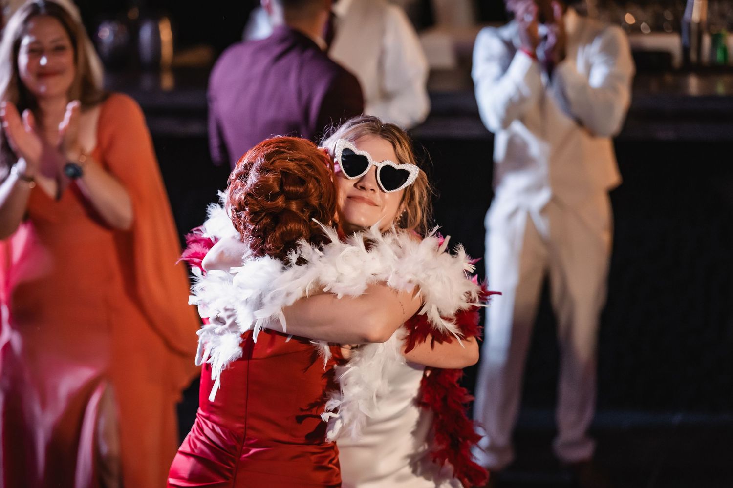 Wedding guests dance and celebrate at a reception with festive feather boas and sunglasses.
