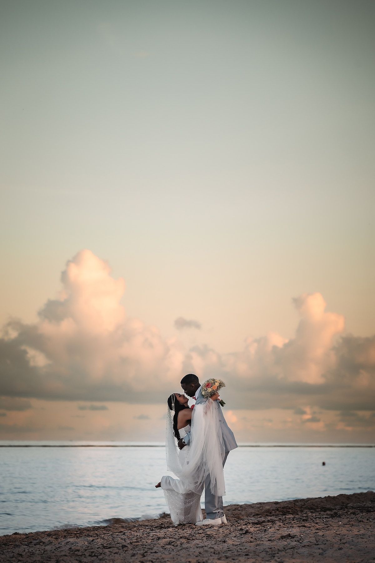 Romantic sunset beach photoshoot with ocean and pastel sky backdrop.