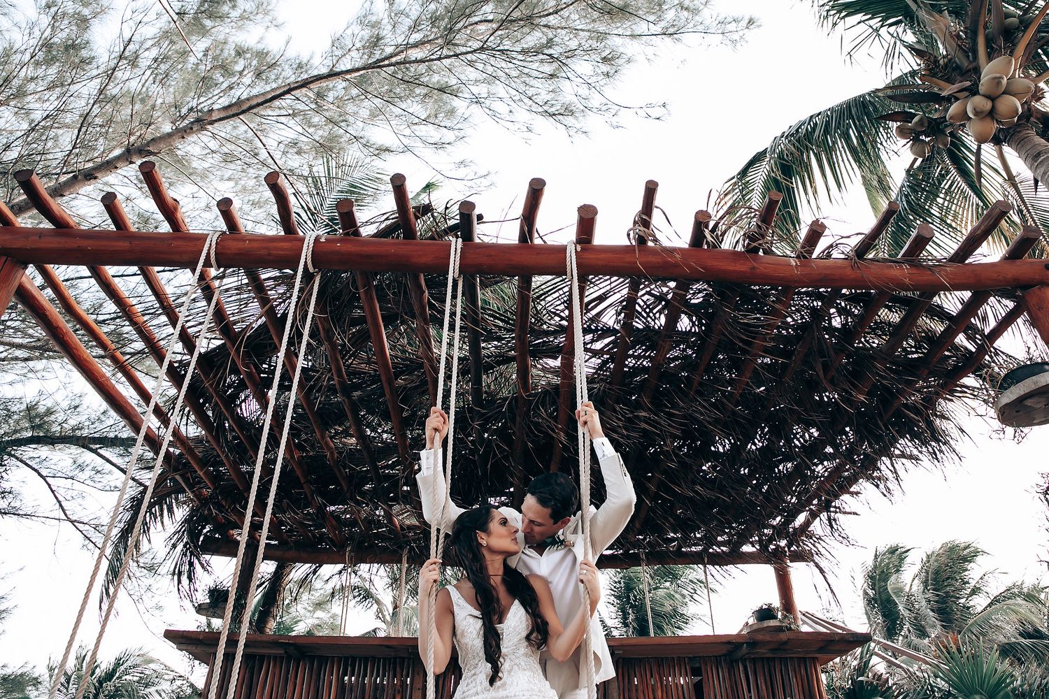 Tropical beach wedding setup with wooden pergola and palm trees swaying in the breeze.